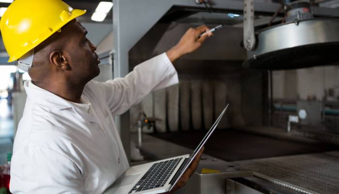Male worker wearing lab coat while using laptop in juice factory